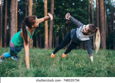 Two female buddies doing partner side plank giving high five while training in the forest - Powered by Shutterstock