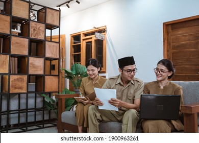 two female civil servants and a male civil servant sit using laptop computers and worksheets while working from home