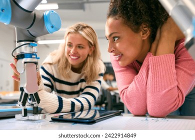Two Female College Or University Engineering Students Using Digital Tablet To Control Robot Arm