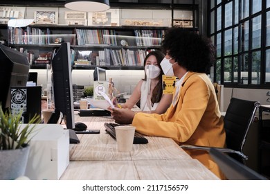 Two Female Coworkers Team With Face Mask Working In New Normal Office. COVID-19 Protection By Cleared Partition, Business Workplace Office, Social Distancing For Pandemic Health, Disease Prevention.