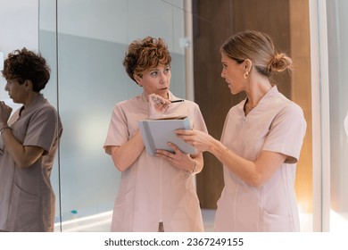 Two female dentist in uniform using a digital tablet and talking in a clinic - Shutterstock ID 2367249155