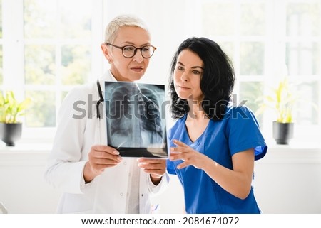 Two female doctors nurses interns caregivers checking discussing diagnosis on x-ray photo of lungs of patient at hospital