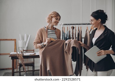 Two female fashion designers discussing clothes while working in workshop together - Powered by Shutterstock