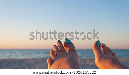 two female feet with painted nails against the backdrop of the sea and sand, pedicure health beauty