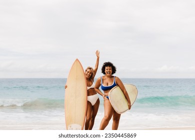 Two female friends celebrating a summer adventure on the beach. Happy women in swimwear cheer excitedly while holding their surfboards on the shore, teaming up for a journey of fun wave riding. - Powered by Shutterstock