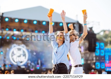 Two female friends drink beer and have fun at the music festival.  Summer holiday, vacation concept.
