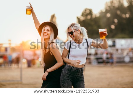 Two female friends drinking beer and having fun at music festival