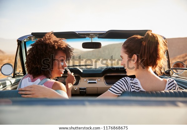 Two Female Friends Enjoying Road Trip In Open Top\
Classic Car