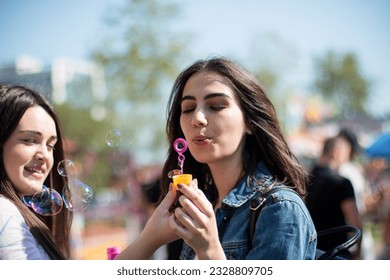 Two female friends hanging out in the amusement park, blowing soap bubbles, having fun together. - Powered by Shutterstock