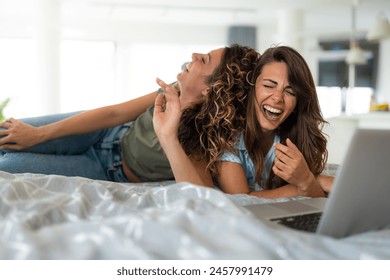 Two female friends laughing while watching funny movie scene. Two young woman enjoying their time at home, laughing hard while watching comedy film. - Powered by Shutterstock