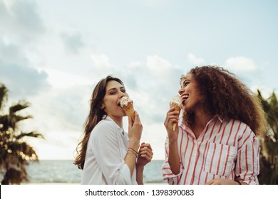 Two Female Friends Licking The Ice Cream Cone. Beautiful Women Enjoying Eating Ice Cream Together Outdoors.