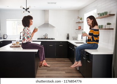 Two Female Friends Meeting For Coffee At Home Sitting On Kitchen Island