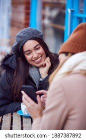 Two Female Friends Meeting Outside Coffee Shop On City High Street Looking At Mobile Phone