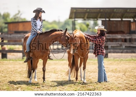 Two female friends on a ranch are getting ready for a horse ride. 
