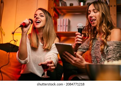 Two Female Friends Sit At Home On Saturday Night And Sing A Duet On Karaoke Night.