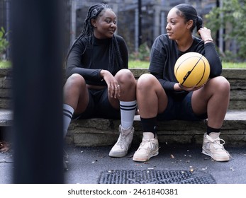 Two female friends sitting outdoors with basketball - Powered by Shutterstock