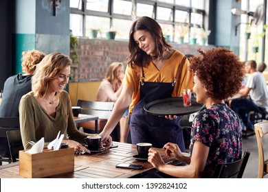 Two Female Friends Sitting At Table In Coffee Shop Being Served By Waitress - Powered by Shutterstock