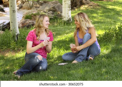 Two Female Friends Sitting Together Playing Cards Outside