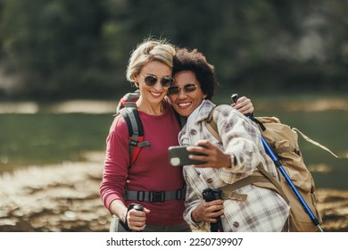 Two female friends taking selfies by a river during a hike along the mountain. - Powered by Shutterstock