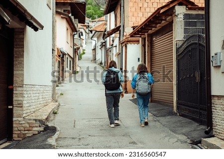Two female friends travelers walking along the narrow streets of a European city along private houses. Travel to Sarajevo, a city in the mountains.