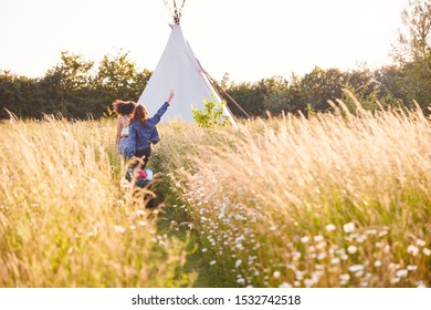 Two Female Friends Walking Pulling Trolley Through Field Towards Teepee On Summer Camping Vacation - Powered by Shutterstock