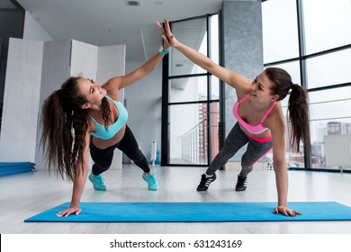 Two Female Friends Wearing Sportswear Giving High Five While Training On Floor In Gym