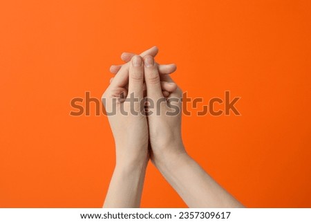 Two female hands clasped on an orange background