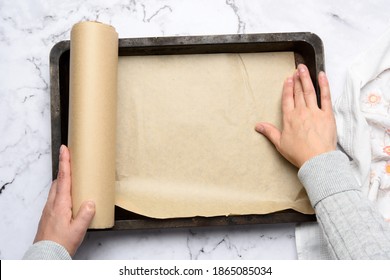 two female hands cover with brown parchment paper an iron rectangular baking sheet, top view