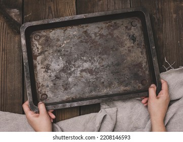 Two female hands hold a rectangular empty baking sheet on a brown wooden table, top view