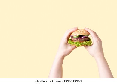 Two female hands holding delicious beef burger on the yellow background, close up.