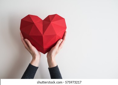 Two female hands holding red polygonal paper heart shape