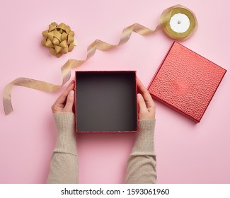 Two Female Hands Holding A Square Empty Gift Box Over A Pink Background, Top View