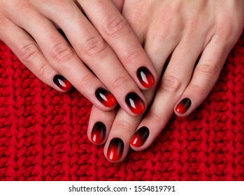 Two female hands with red black ombre gradient nails on knitted fabric. Trendy winter manicure concept.