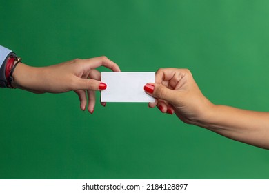 Two female hands wearing red nail polish, giving white business card. Green background.
