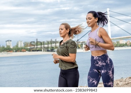 Two female joggers pursuing their activity outdoors by the river shore.