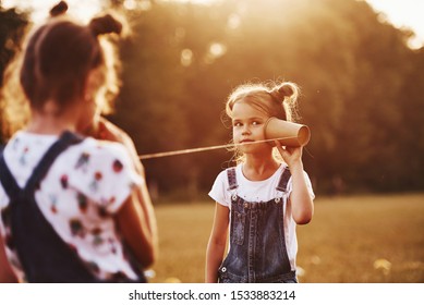 Two Female Kids Stands In The Field And Talking By Using String Can Phone.