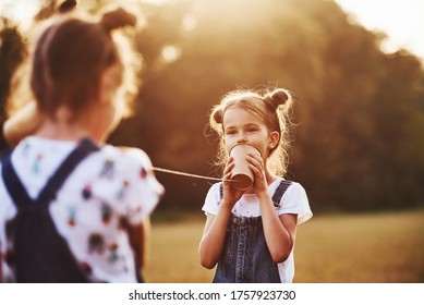 Two Female Kids Stands In The Field And Talking By Using String Can Phone.