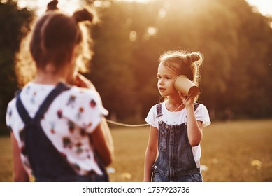 Two Female Kids Stands In The Field And Talking By Using String Can Phone.