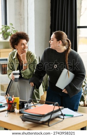 Two female managers discuss work while enjoying a moment in a vibrant office setting.