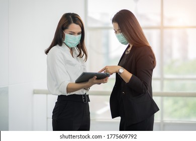 Two female office workers in business suit wears facemask and discuss about their work via tablet in business building. Businesswoman talking and poitning on tablet. Business stock photo - Powered by Shutterstock