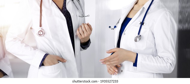 Two female physicians are discussing medical therapy, while standing at the table in a clinic office. Doctors use pc computer at work. Teamwork in medicine