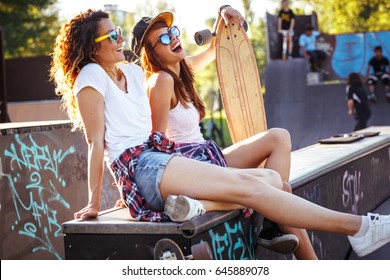 Two Female Skaters Friends Sitting  On Ramp  And Hangout At The Skate Park .Laughing And Fun.