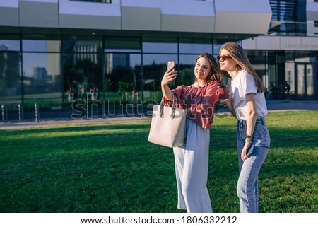 two female students take a photo on their phone while walking near the building.