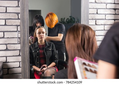 Two Female Stylists Standing And Picking A Color For Hair Dyeing Behind Young Woman Sitting In Chair In Beauty Salon