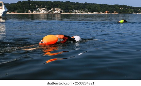 Two female swimmers swimming in Centerport Harbors Fleets Cove wearing colorful safety buoys floating behind them. - Powered by Shutterstock