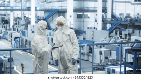 Two Female Technicians in Protective Coveralls Having a Conversation and Using Tablet Computer. Specialists Monitoring, Analyzing Conditions at a Modern Electronics Factory with Automated Robots - Powered by Shutterstock