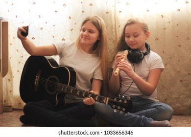 Two female teens playing musical instruments and making selfie sitting on the floor at home