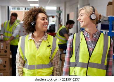 Two Female Workers Using Headsets In Distribution Warehouse