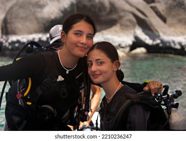 Two Female Young Scuba Diver Sisters On A Diving Boat In Thailand Portrait Looking Into The Camera With Full Gear Attached