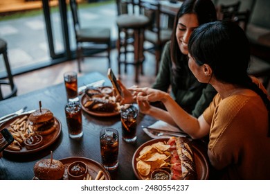 Two females eating in the restaurant and looking and commenting something from a smartphone together - Powered by Shutterstock